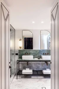 Modern bathroom with marble tiles, white sinks, and black metal accents.
