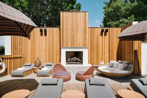 A modern outdoor lounge area featuring wooden panels, concrete base, and wicker furniture with cushions.