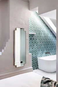 Modern bathroom interior with green and white geometric tiles, white freestanding bathtub, and minimalist design elements.