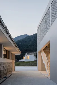 Modern residential exterior featuring concrete and wood materials, with a mountainous background.