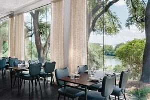 A modern restaurant interior featuring glass windows with a scenic view of trees and water.