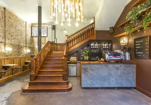 A cafe interior with wooden stairs, concrete flooring, and plants.