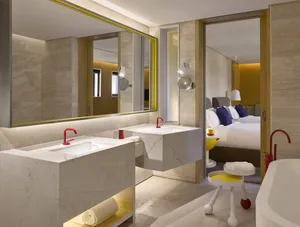 Modern minimalist bathroom with a white marble sink, taupe walls, and a yellow stool.