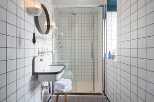 Modern minimalist bathroom with white tiled walls and glass shower enclosure, featuring a simple sink and towel rack.