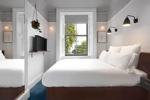 A minimalist bedroom featuring a white bed with a wooden headboard, white textiles, and minimalist decor.