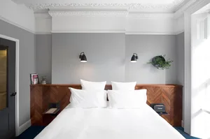 A minimalist bedroom with a white bed, wooden headboard, and black wall-mounted lamps.