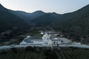 Aerial view of a modern residential building with white concrete exterior surrounded by green mountains.