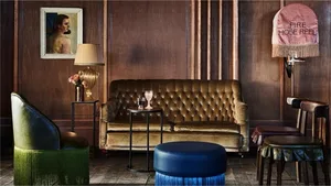 A cozy, industrial-themed living room featuring a plush, green-fringed leather sofa, wooden furnishings, and rustic elements 