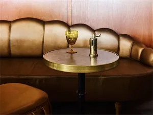A round brown leather table with a glass and a brass lighter on top, against a brown leather background.