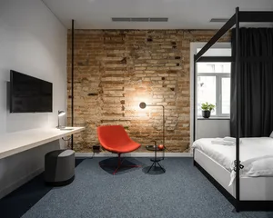 A minimalist bedroom featuring a red chair, a modern bed, and a brick wall.