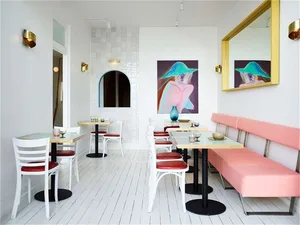 A modern cafe interior with minimalist design features, including white walls, pink seating, and minimalist furniture.