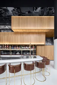 A modern bar interior with wooden cabinets, leather stools, and brass accents.