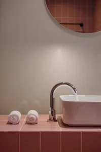 Modern bathroom with a sink, faucet, and three white towels on a pink tiled countertop.