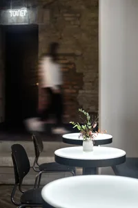 A modern cafe interior featuring minimalist round tables with white surfaces and black legs, illuminated by ambient lighting,