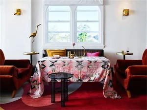 A contemporary living room featuring a patterned textile tablecloth, red velvet chairs, and brass accents.