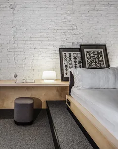 A modern minimalist bedroom featuring a wood frame bed with white bedding, a wooden nightstand with a round footstool, and fr
