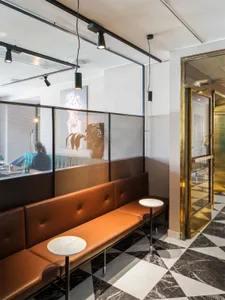 A minimalist restaurant interior featuring a leather bench, marble floor, and metal railings.