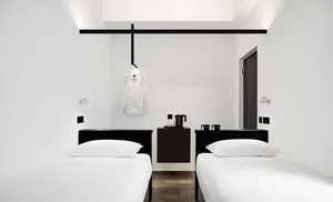 Two single beds with white bedding in a minimalist hotel bedroom.