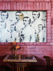 A restaurant interior with a pink brick wall featuring a poster of men in suits with flowers in their hair.
