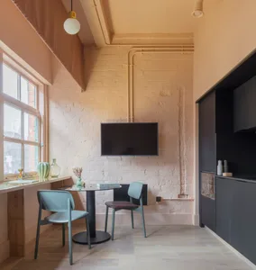 A modern industrial living room with a black table, green chairs, and a brick wall.