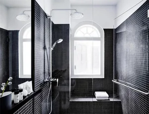 A modern, minimalist bathroom with black tiled walls and floor, a walk-in shower, and a window with an arched top.