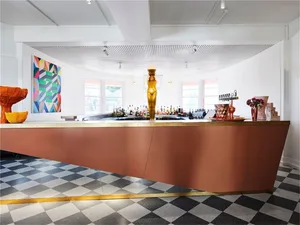 A modern bar interior featuring a metallic and wooden counter with a geometric art piece on the wall.