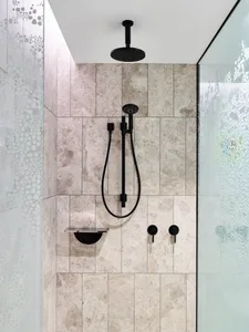 A modern bathroom shower with light brown marble tiles and black fixtures.