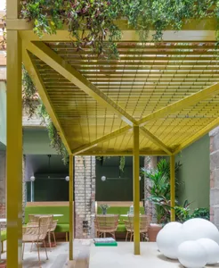 Modern cafeteria with green metal pergola, potted plants, and green seating areas