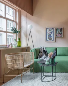 A modern living room with a green sofa, a rattan chair, and a small side table with a vase of flowers.