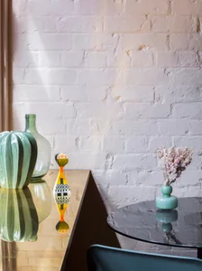 A living room with a glass side table featuring decorative items and a vase of flowers.