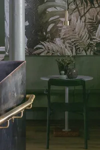 A modern living room with greenery accents, featuring a dark green wall, a white side table with a flower arrangement, and a 