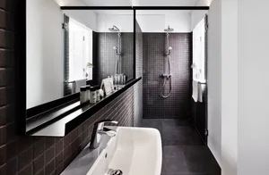 Modern minimalist bathroom featuring black and gray square tiles, a sleek white sink, and a walk-in shower with a rain shower
