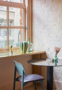 A minimalist window-side table with a wooden frame, glass tabletop, and a green plant and vase on display.