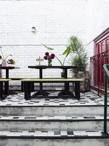 Outdoor seating area with black tables, green benches, and checkered black and white tiles on the floor.