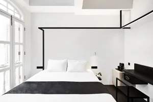Modern minimalist bedroom with a single white bed featuring a black textile cover and metal headboard.