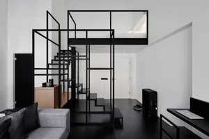 A minimalist living space with a metal staircase and metal walls, featuring a grey couch, a desk, and a loft bed.
