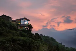 Modern house with glass walls and steel structure on a hillside at sunset.