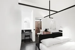 Modern minimalist bedroom with white walls, black furniture, and white bedding.