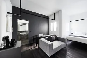A modern minimalist bedroom with black, white, and gray tones featuring a simple sofa, a bed with a black and white comforter