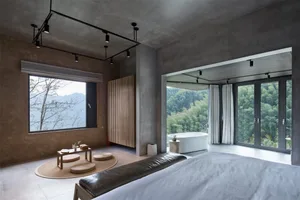A minimalist bedroom with concrete walls and a view of the mountains through the large windows.