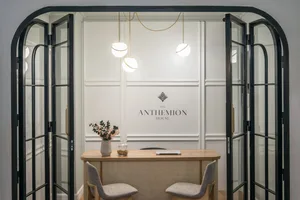 Modern minimalist office reception area with glass and wooden surfaces, potted plant, and hanging lights.