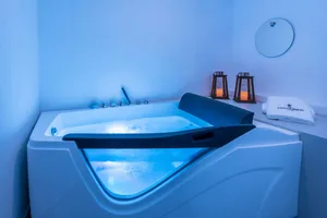 An image of a spa bathroom featuring a modern indoor thermoplastic lavatory bath with blue lighting and porcelain fixtures.