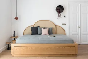 A modern bedroom with a light wood bed, featuring a woven headboard and colorful pillows.