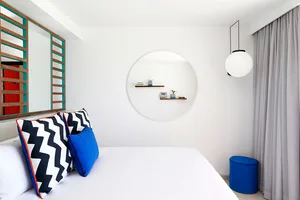 Minimalist bedroom with white walls, blue and black geometric pillows on a bed, and a hanging globe light fixture.