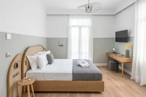 A modern, minimalist bedroom featuring a wooden frame bed with white bedding and grey accents, situated in a room with grey a