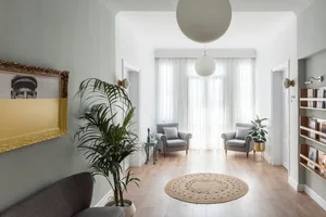 A minimalist modern living space with a wooden floor, gray armchairs, and glass windows.