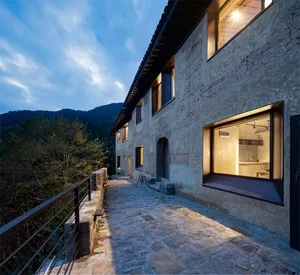 A modern residential exterior with concrete walls, large windows, and a stone path leading to the entrance.