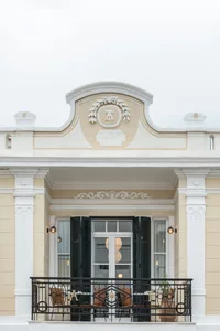 Facade of a building with concrete walls, black shutters, and an ornate logo above the door.