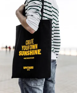 Person holding a black tote bag with 'CREATE YOUR OWN SUNSHINE' text on it.
