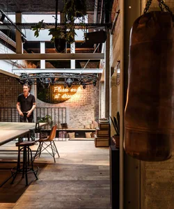 Industrial-style interior space featuring exposed brick, concrete walls, wooden elements, and a neon sign encouraging kindnes